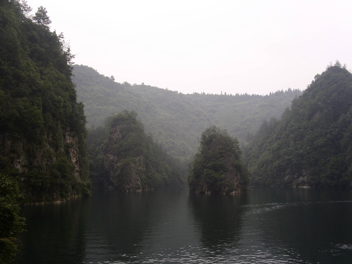 Baofeng Lake with a forested rocky islet rising from calm water on a misty day