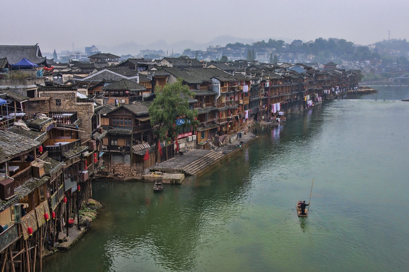 Wooden stilt houses of Fenghuang Ancient Town lining the Tuo River, with a boatman poling a small boat