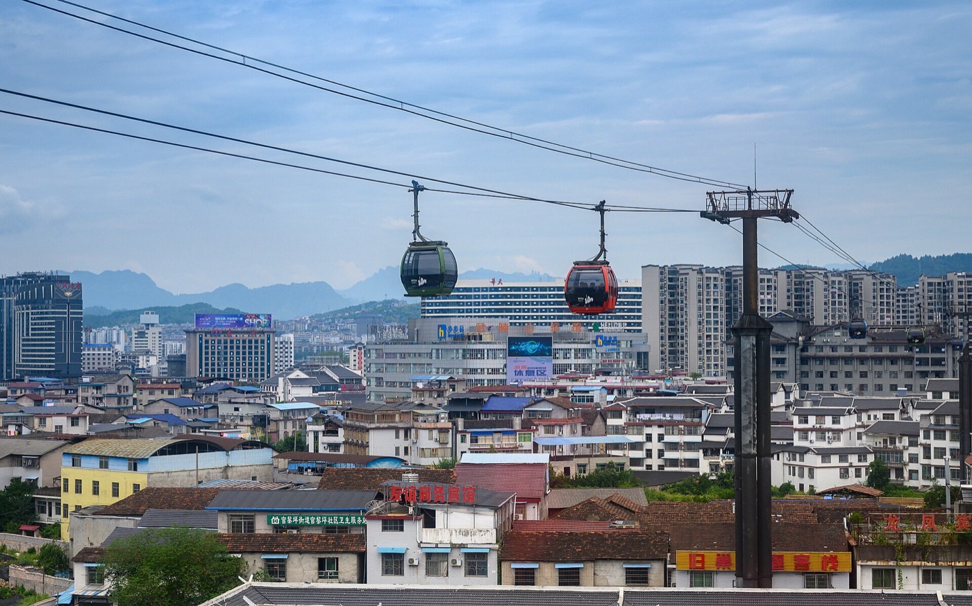 Tianmen Mountain cableway gondolas passing over rooftops of Zhangjiajie city, with mountains in the distance